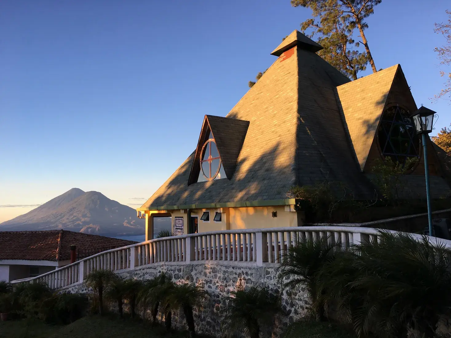 Die Pyramide Paz Mundo im Abendlicht, dahinter ein Vulkan am Atitlánsee